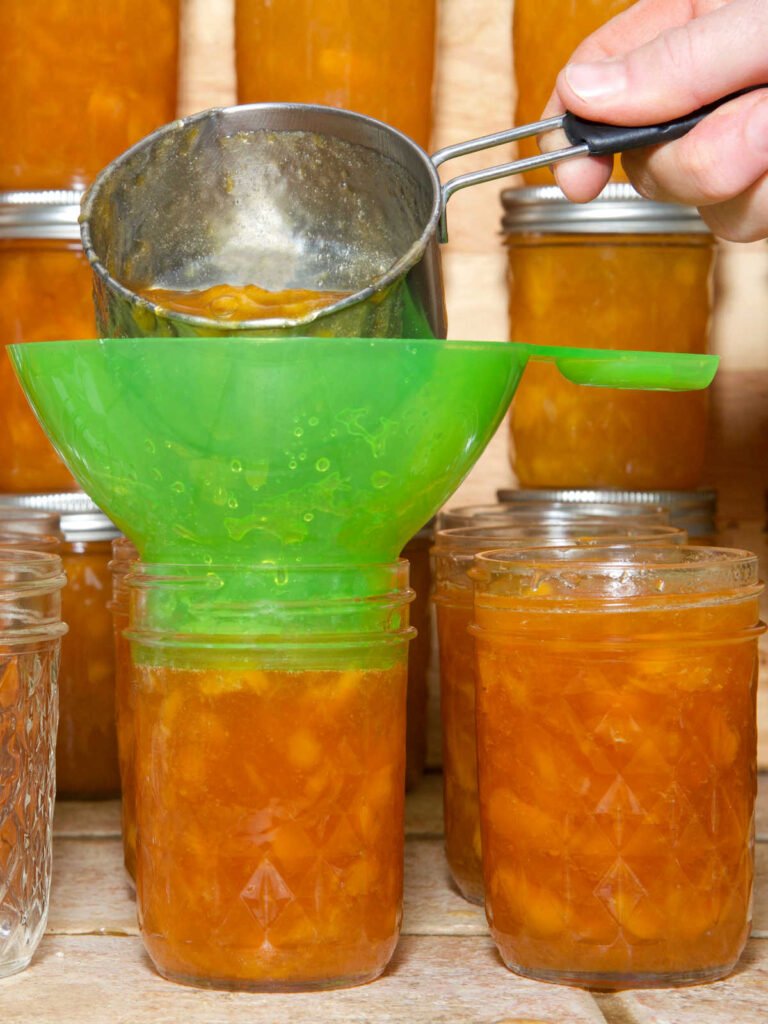 soup ladled into green funnel that is in a jar filled with the soup.  Canning jars surrounding that jar all full of the same soup.