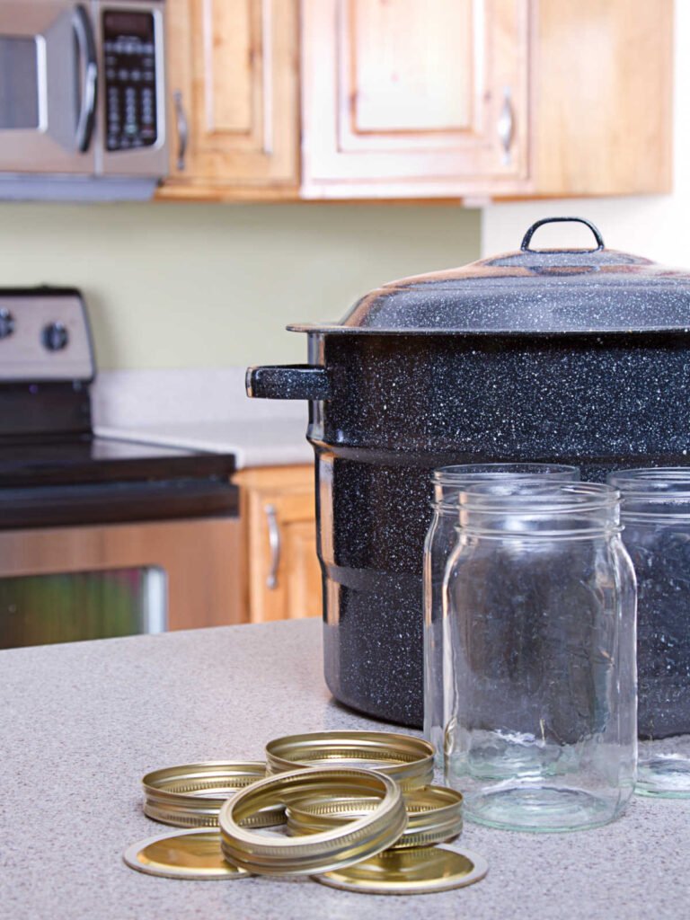 water bath canner, a couple mason jars in front of it with a pile of lids and bands next to them.