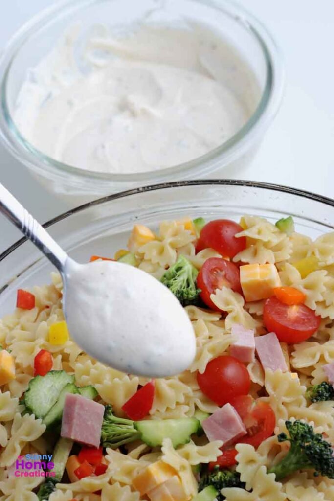 small bowl of dressing in background, spoon with dressing over top of pasta salad.