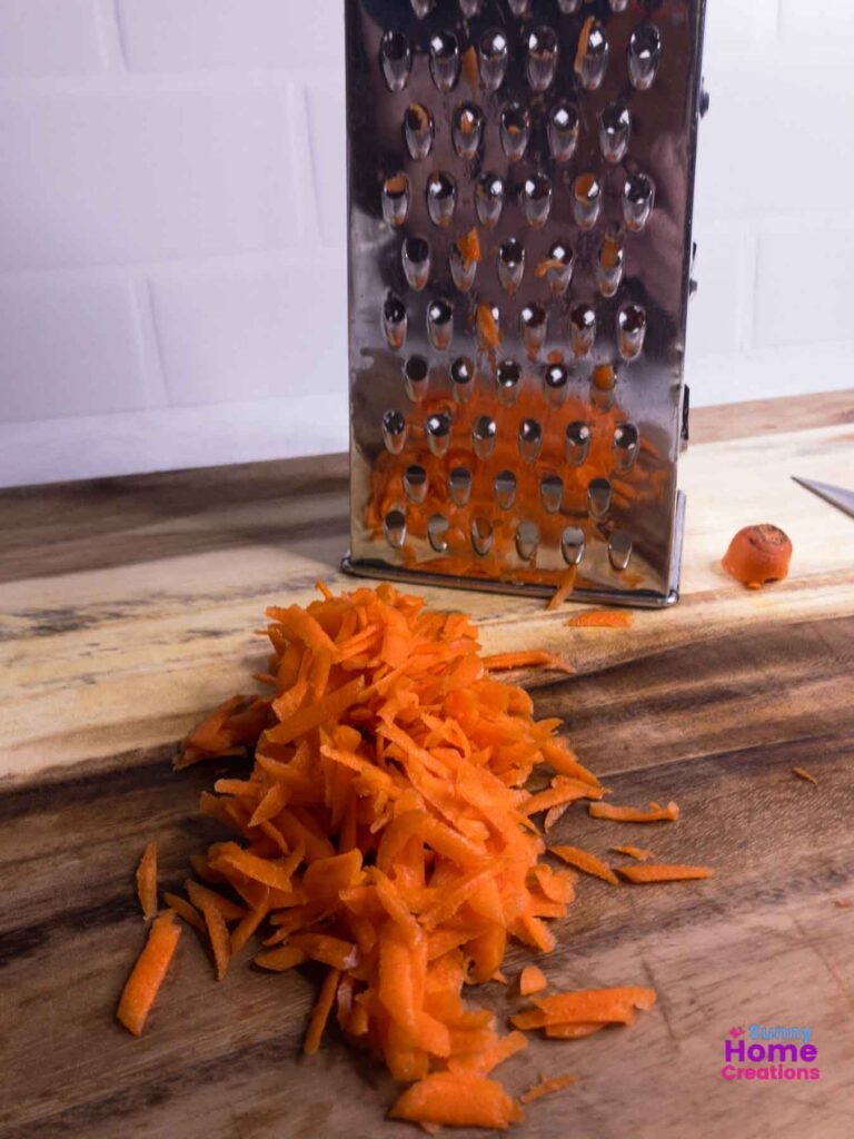 shredded carrots on cutting board with grater in background.