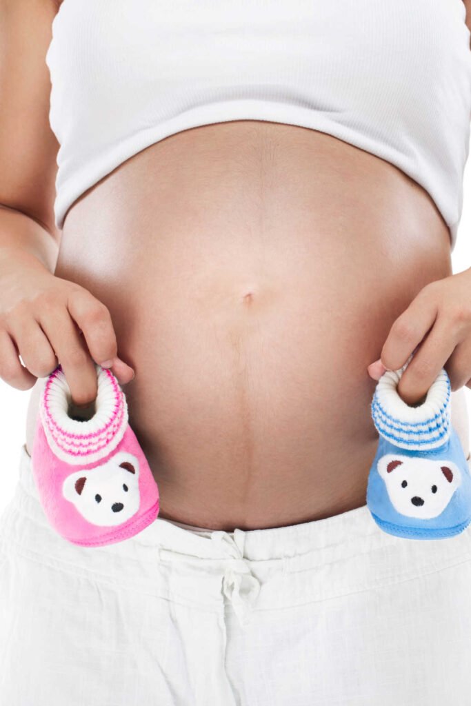 Woman holding up one boy and one girl bootie on each side of pregnant belly.